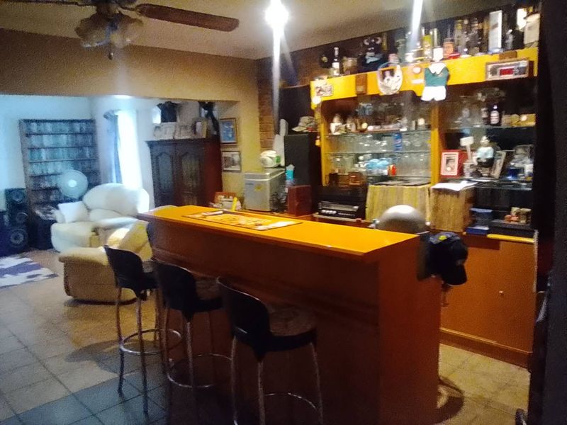 A home bar area featuring a built-in wooden bar counter and integrated shelving, with tiled flooring and a ceiling fan.