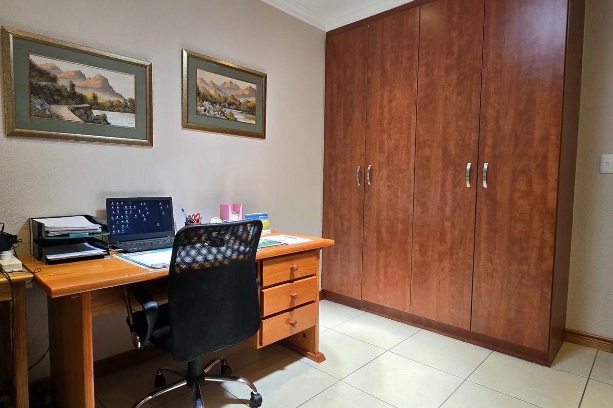 A functional bedroom or home office space featuring built-in wooden cupboards and tiled flooring.