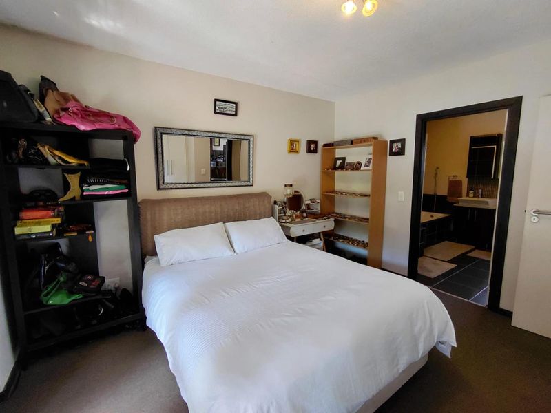 A carpeted bedroom featuring an en-suite bathroom entrance, neutral wall tones, and a functional layout with direct access to the adjoining bathroom.