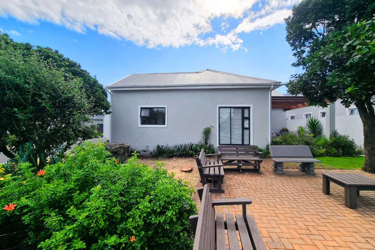 A well-maintained rear exterior view of the house featuring a paved patio area, landscaped garden, and modern grey facade with white-framed windows.