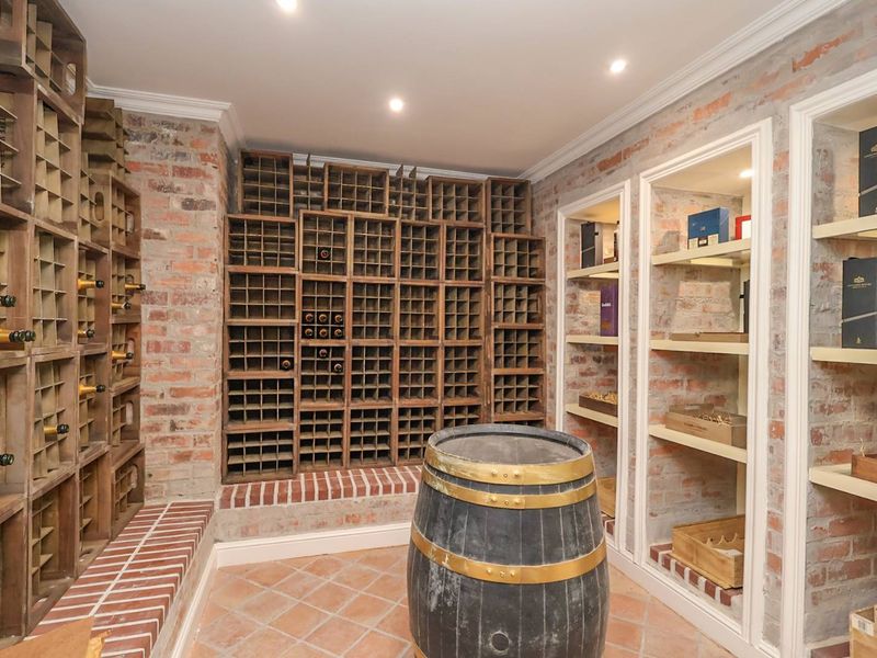 A dedicated wine cellar featuring extensive built-in timber wine racking, exposed brick walls, and terracotta flooring, providing a classic storage environment for wine collections.