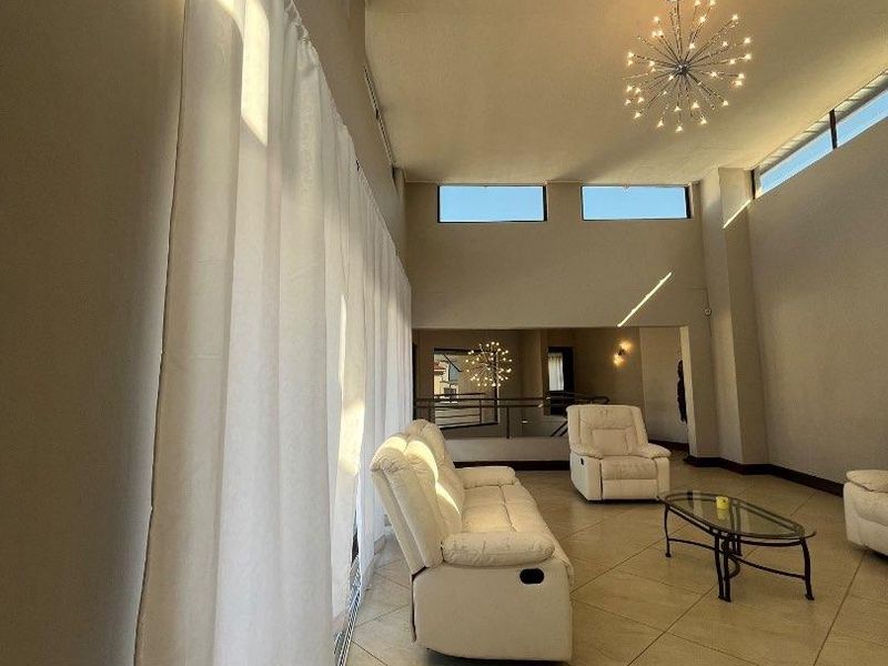 Spacious living room featuring high ceilings, clerestory windows for natural light, tiled flooring, and a contemporary chandelier.