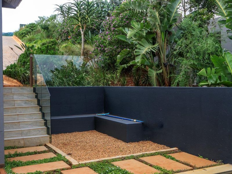A well-maintained garden area featuring a stone staircase with a glass balustrade, a built-in bench, and landscaped terraced planting.