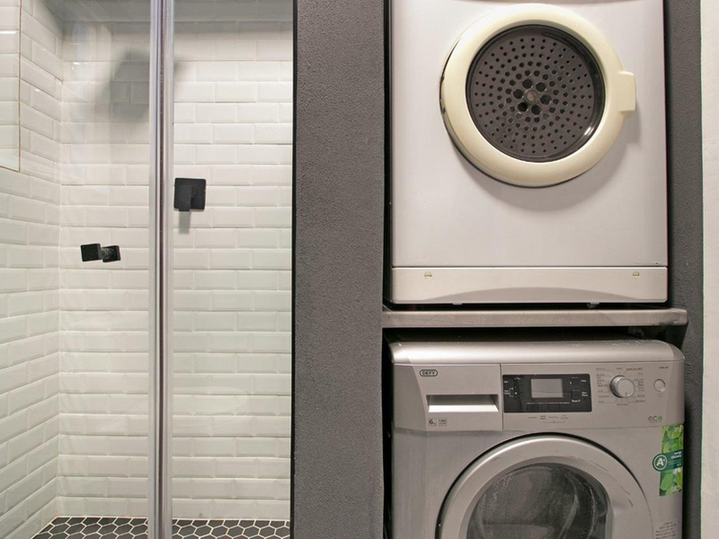 A compact laundry area featuring a stacked washing machine and tumble dryer, adjacent to a modern shower with subway tiling and hexagonal floor tiles.