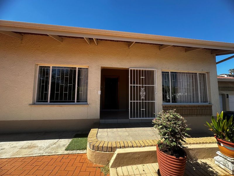 Front facade of the house featuring a tiled entrance, security gate, and brick paved walkway under a roof overhang with exposed rafters.