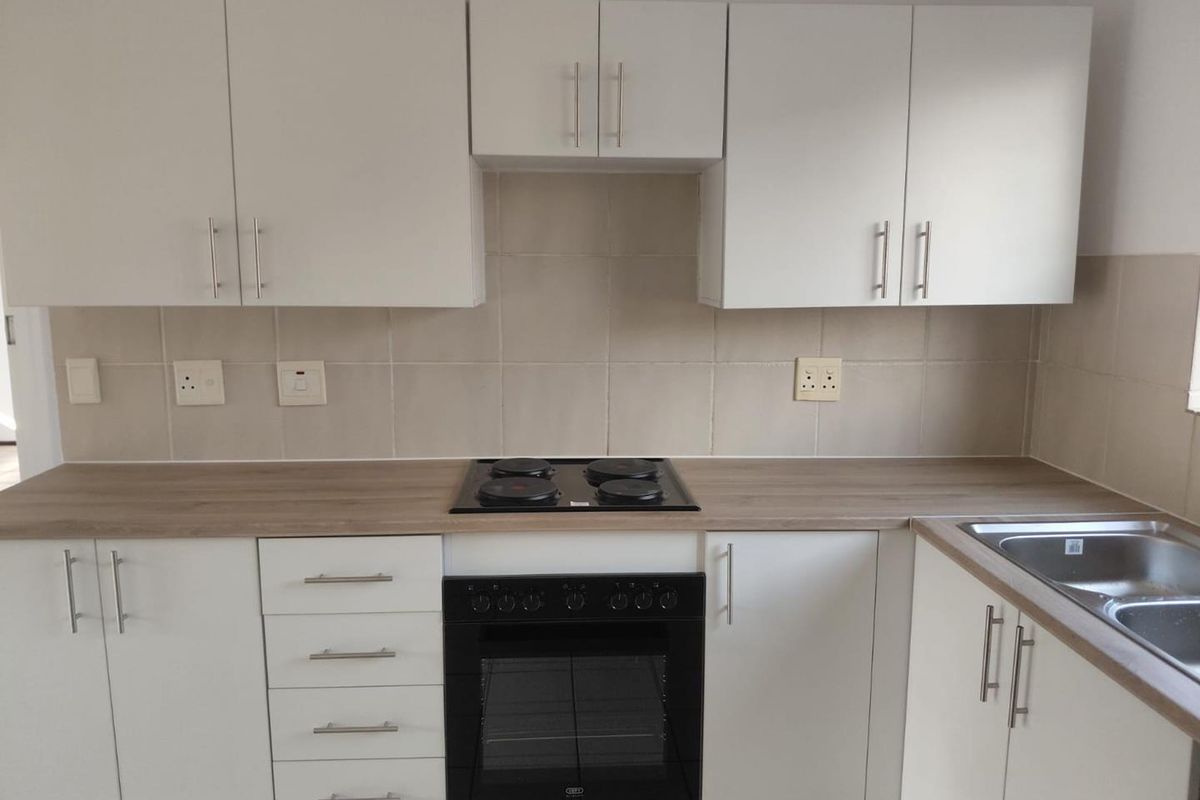 A clean, modern kitchen featuring white cabinetry, wood-look laminate countertops, a built-in oven, electric hob, and a stainless steel sink with tiled splashback.