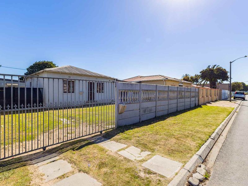 Front exterior view of a single-story house featuring a precast concrete boundary wall, metal gate, and a tiled roof.