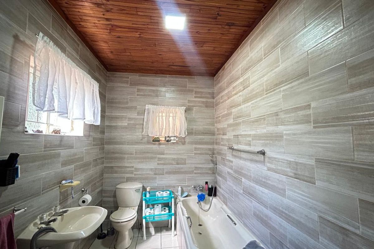 A functional bathroom featuring full-height wall tiling, a bathtub with shower attachment, a pedestal basin, and a timber-paneled ceiling.