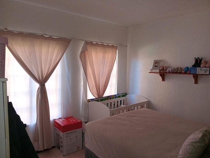 A bedroom featuring natural light through dual windows with curtain rails and a fixed wall-mounted display shelf.