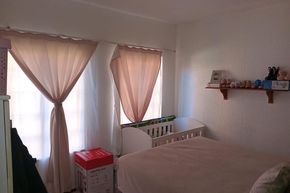 A bedroom featuring natural light through dual windows with curtain rails and a fixed wall-mounted display shelf.