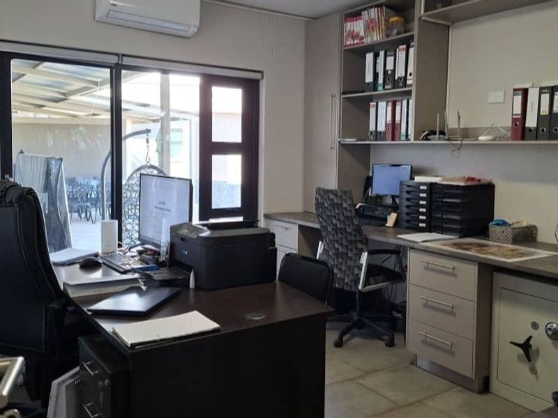 A functional home office featuring built-in cabinetry, shelving, a secure wall safe, tiled flooring, and direct access to an outdoor patio area.