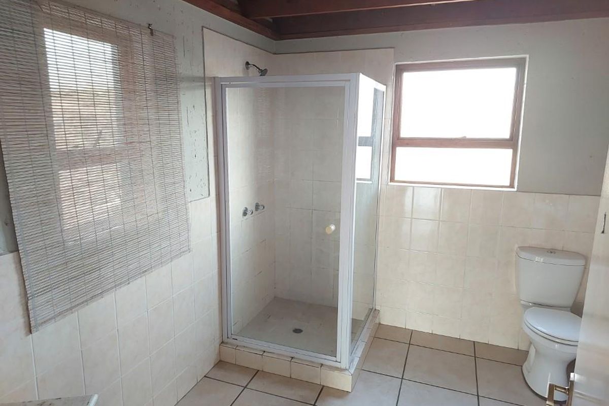 A functional bathroom featuring a glass shower enclosure, toilet, tiled walls and flooring, and exposed timber ceiling beams.