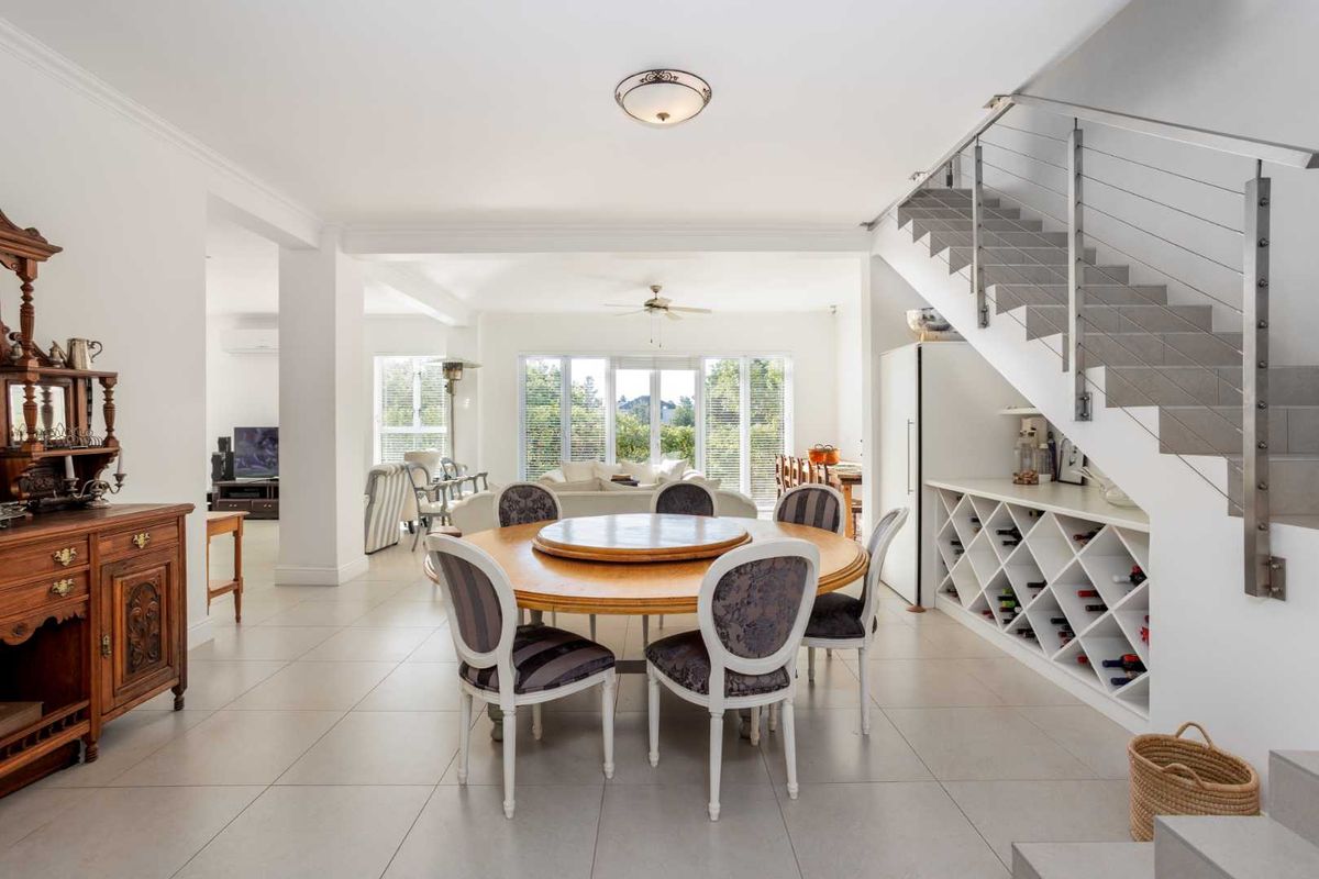 Spacious open-plan living and dining area featuring tiled floors, a modern staircase with cable railing, and a custom built-in wine rack.