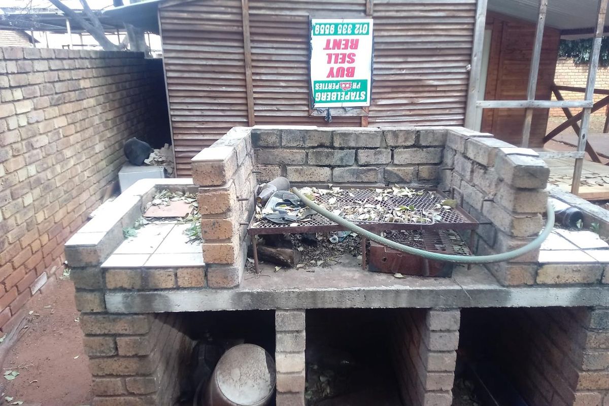 Outdoor brick-built braai area featuring a built-in grill and preparation counter, situated in a rear garden setting.