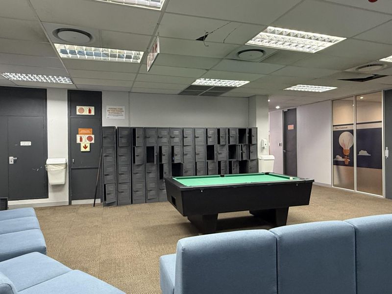 A communal office break area featuring metal lockers, carpeted flooring, and a suspended ceiling with recessed lighting.