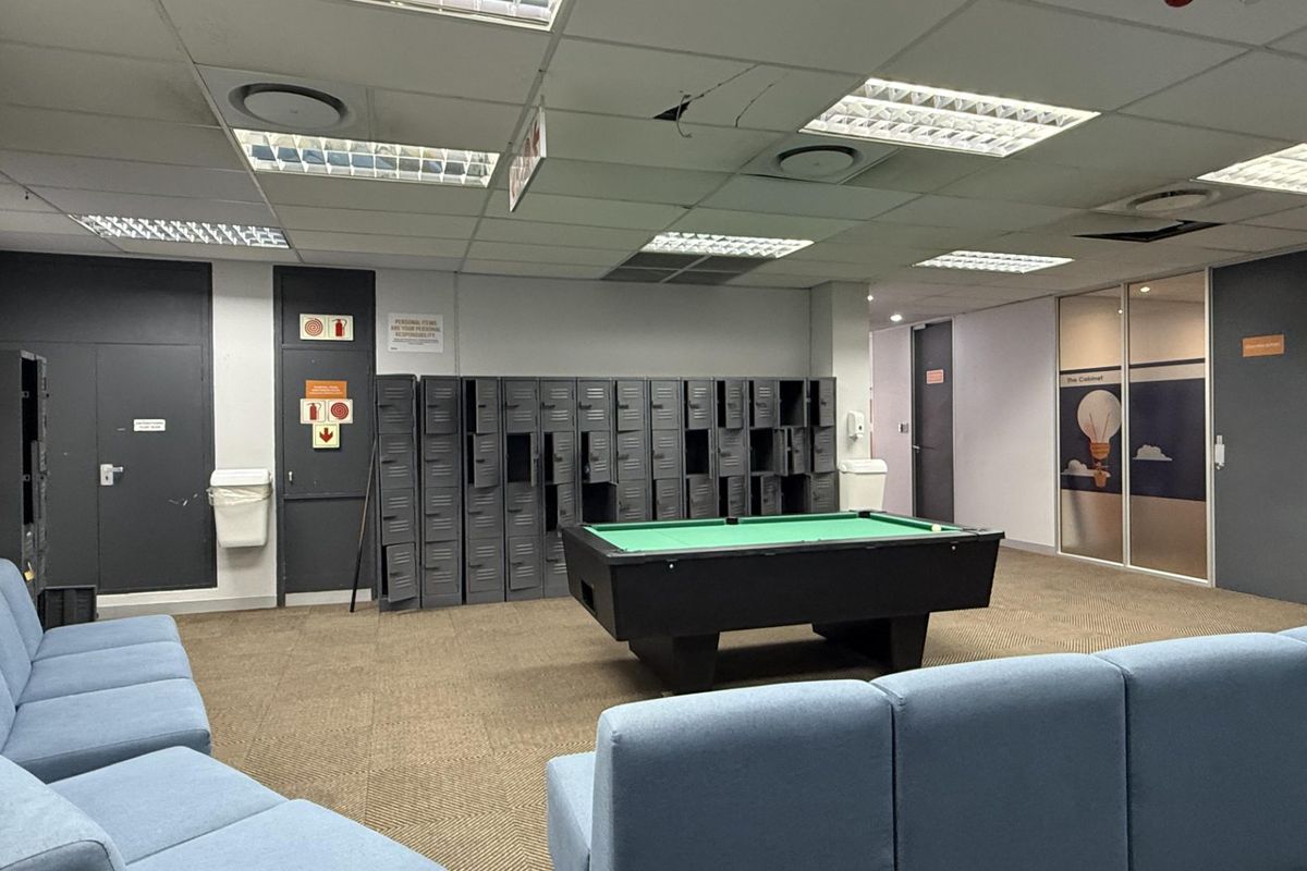 A communal office break area featuring metal lockers, carpeted flooring, and a suspended ceiling with recessed lighting.