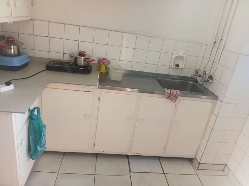A compact kitchen featuring a stainless steel sink, tiled backsplash, and basic built-in cabinetry with tiled flooring.