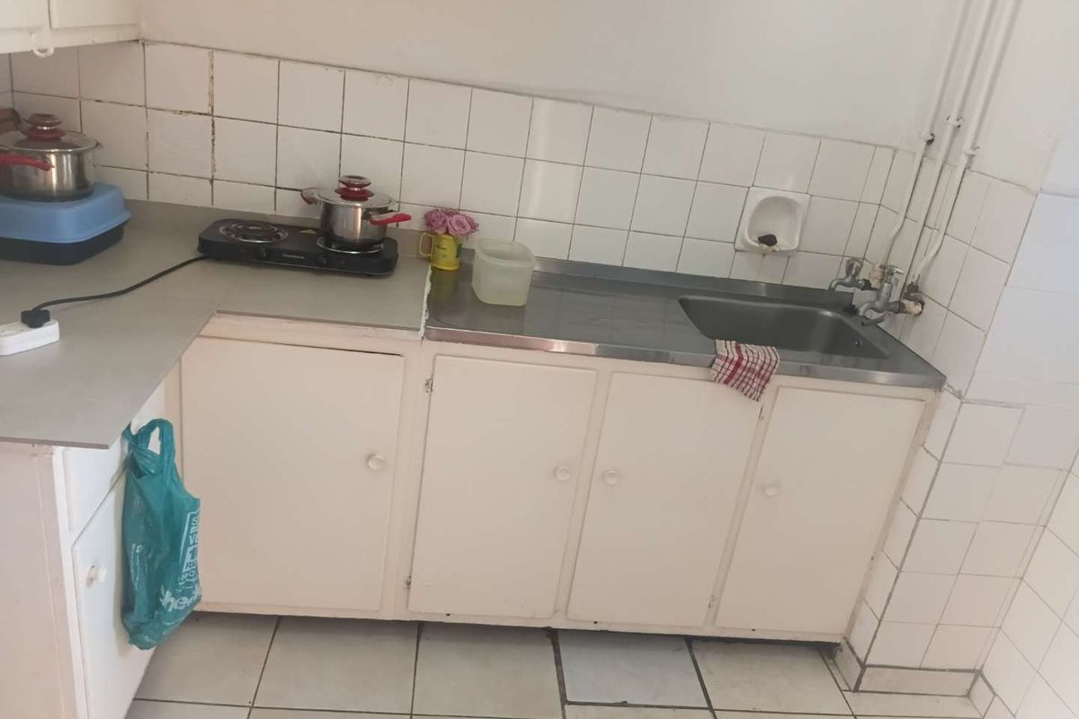 A compact kitchen featuring a stainless steel sink, tiled backsplash, and basic built-in cabinetry with tiled flooring.