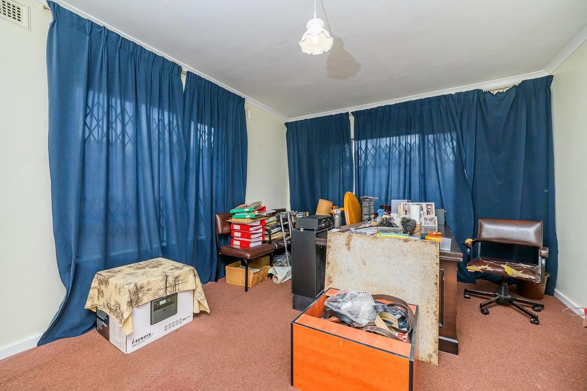 A bedroom featuring carpet flooring, security gates on windows, and a central ceiling light fixture, currently utilized as a home office space.