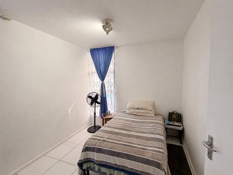 A compact bedroom featuring tiled flooring, a security gate on the window, and a ceiling-mounted spotlight fixture.