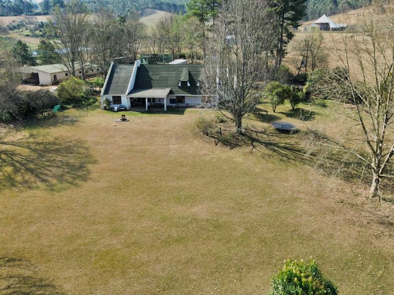 Aerial view of a farm property featuring a main residence with a tiled roof, covered patio, and expansive surrounding grounds.