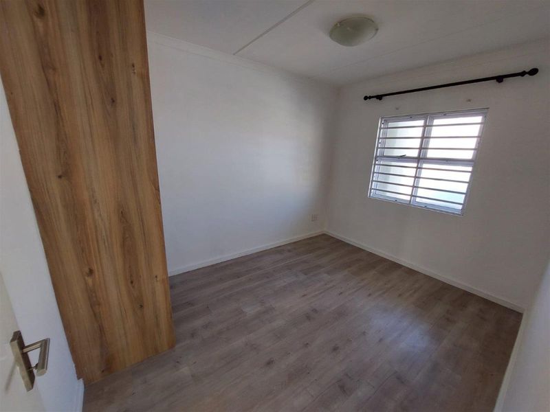 A clean, empty bedroom featuring modern laminate flooring, a built-in wardrobe, and a window fitted with security bars.