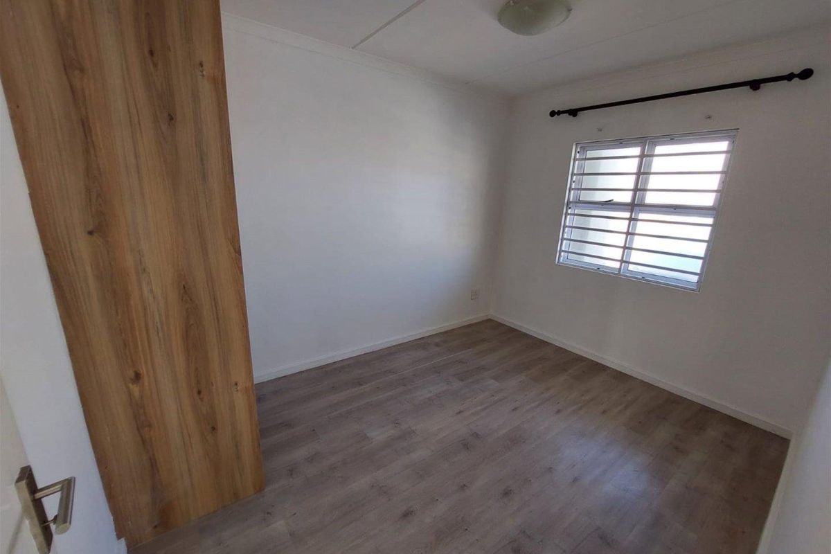 A clean, empty bedroom featuring modern laminate flooring, a built-in wardrobe, and a window fitted with security bars.