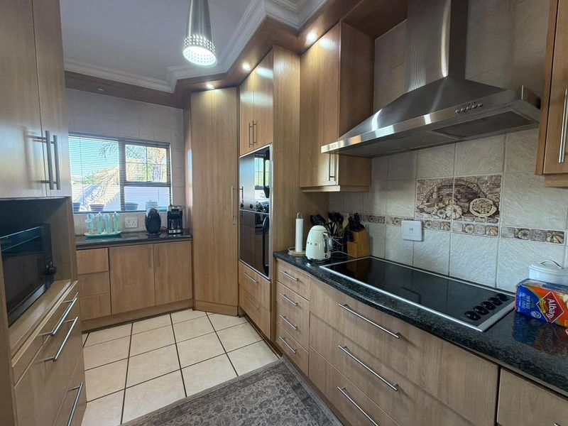 A functional kitchen featuring wood-finish cabinetry, granite countertops, a built-in oven, and a stainless steel extractor fan with tiled flooring.