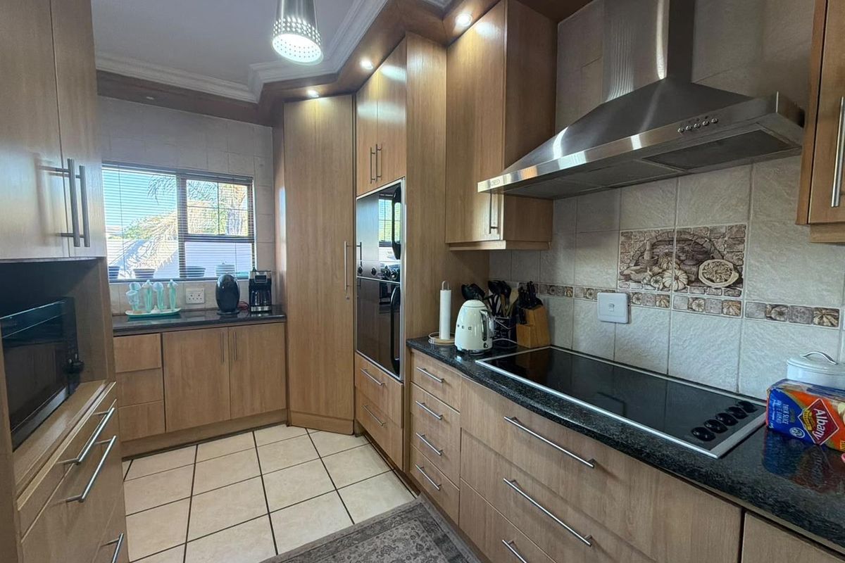 A functional kitchen featuring wood-finish cabinetry, granite countertops, a built-in oven, and a stainless steel extractor fan with tiled flooring.