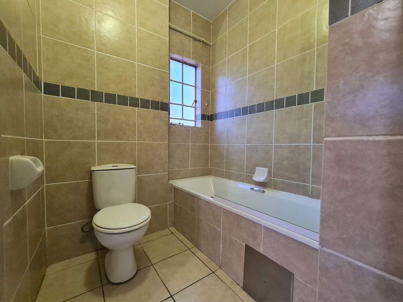 A functional bathroom featuring a bathtub, toilet, and full-height ceramic wall tiling with a decorative border.