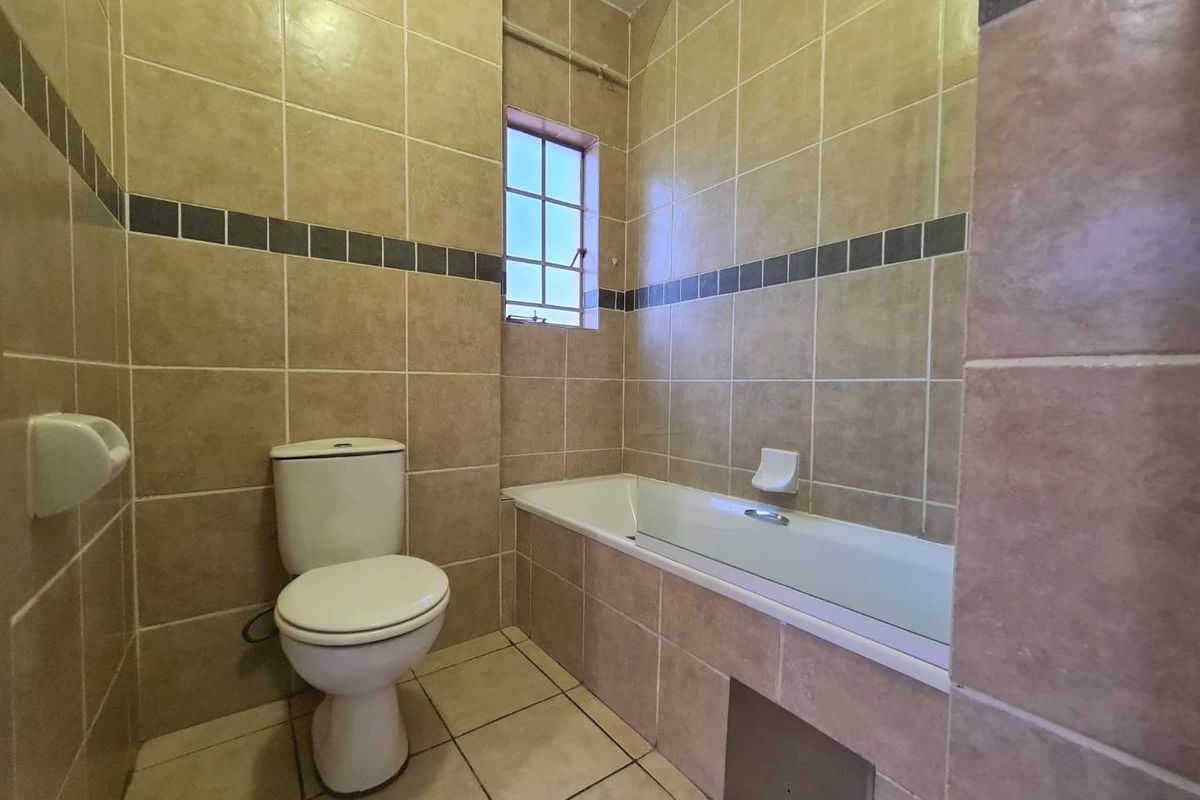 A functional bathroom featuring a bathtub, toilet, and full-height ceramic wall tiling with a decorative border.