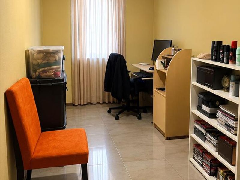 A functional office space featuring neutral tiled flooring, yellow painted walls, and a window with curtains, providing a versatile area for work or study.