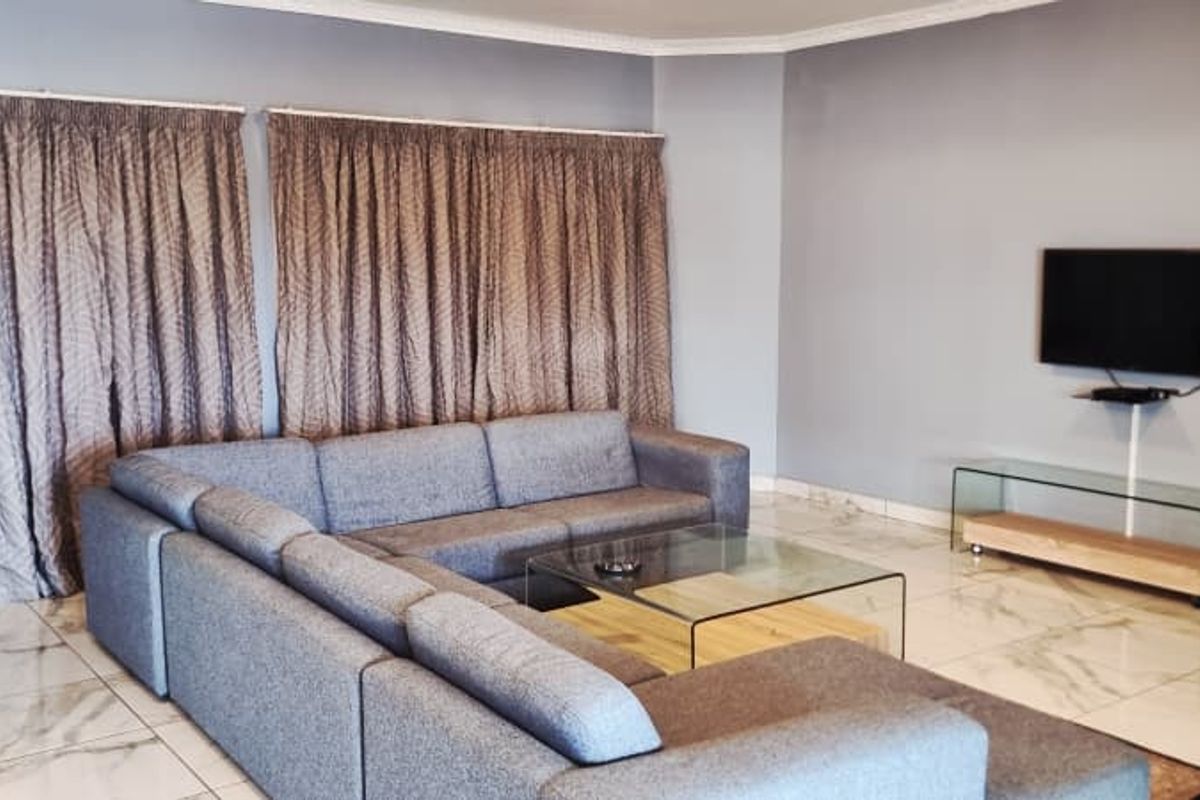 A spacious living room featuring large format marble-look floor tiles, neutral wall tones, and floor-to-ceiling window treatments.