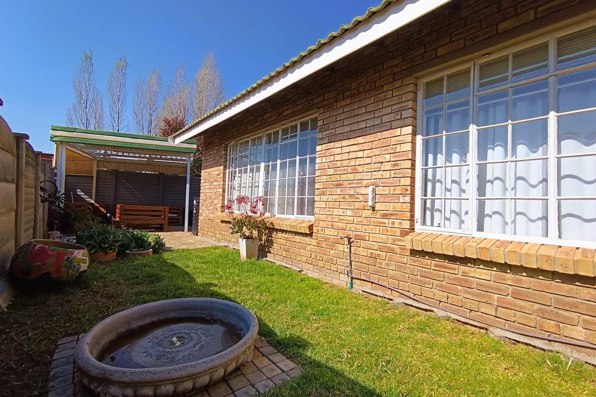 A view of the rear exterior featuring a brick facade, large windows, a small lawn area, and a covered patio structure.