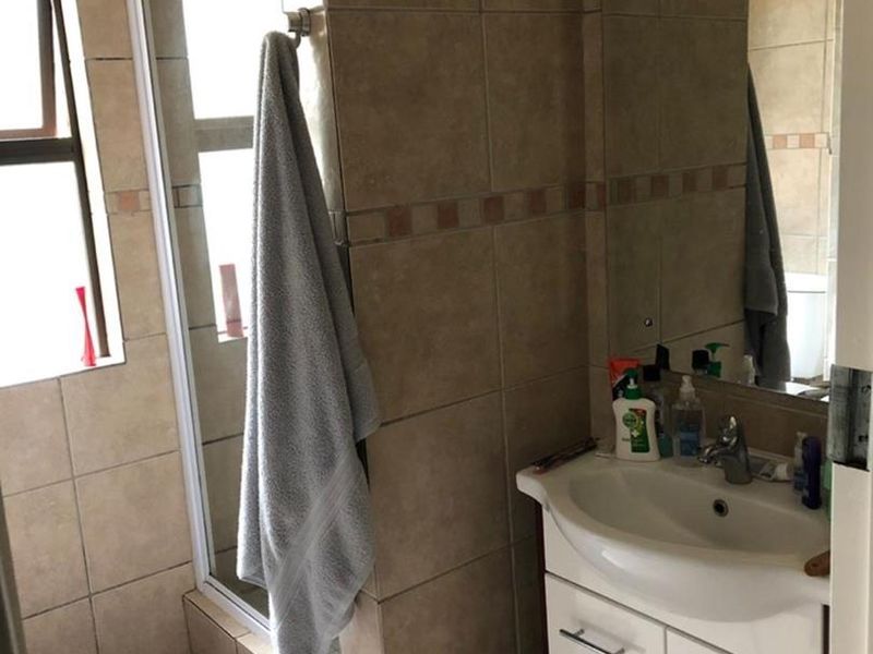 A functional bathroom featuring a shower enclosure, a vanity cabinet with a basin, and neutral wall tiling.