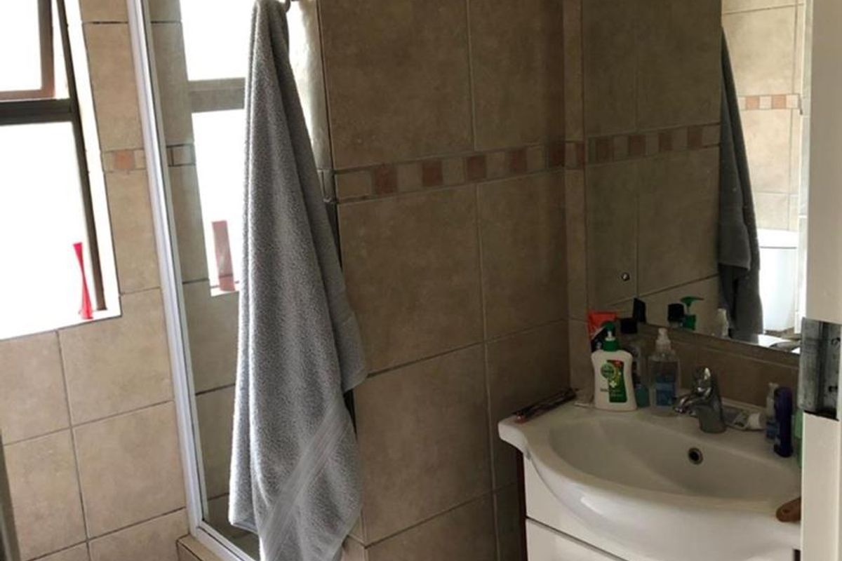 A functional bathroom featuring a shower enclosure, a vanity cabinet with a basin, and neutral wall tiling.