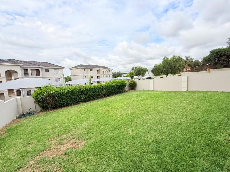 A well-maintained communal garden area featuring a manicured lawn, perimeter boundary walls, and established hedging within an apartment complex.