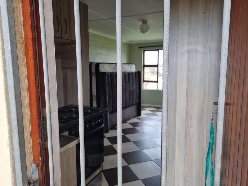 Open plan living area featuring tiled flooring, built-in cabinetry, and a stove, viewed through a security gate.