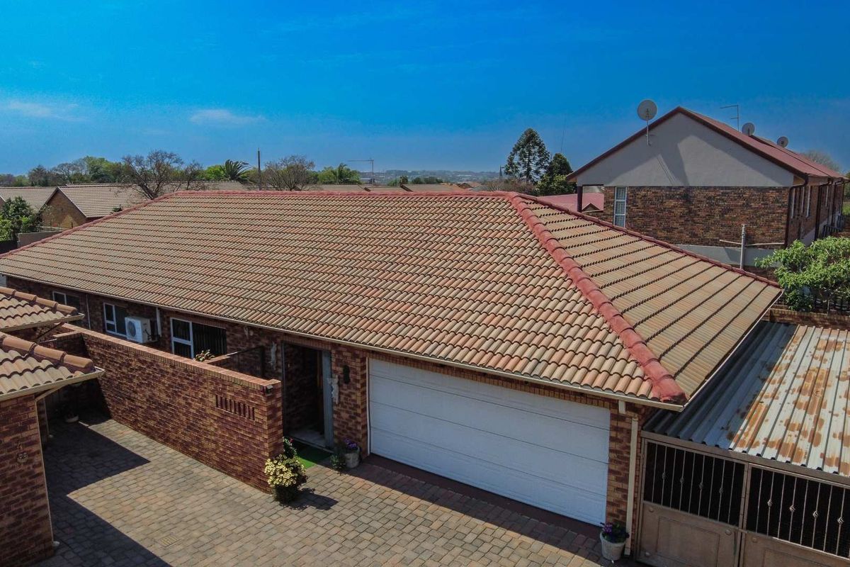 Aerial view of a cluster home featuring a tiled roof, brick facade, paved driveway, and a white sectional garage door.