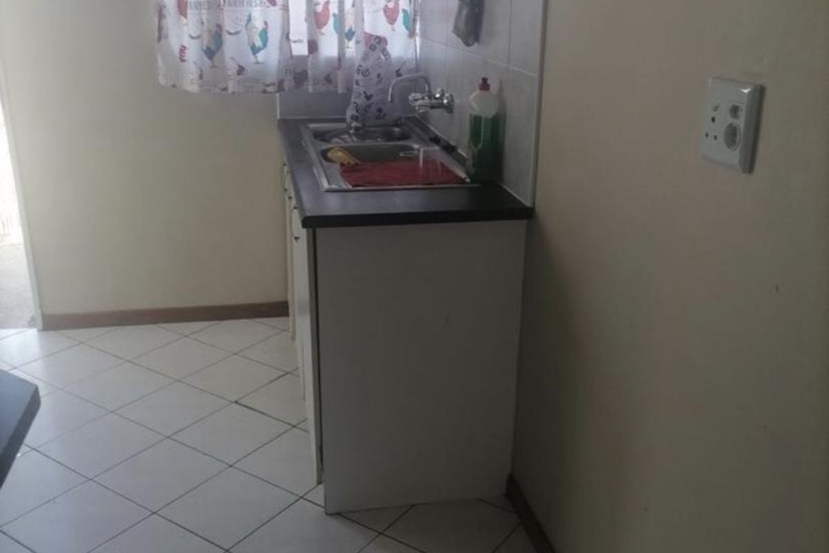 A compact kitchen area featuring tiled flooring, a single sink unit with a tiled splashback, and basic cabinetry.