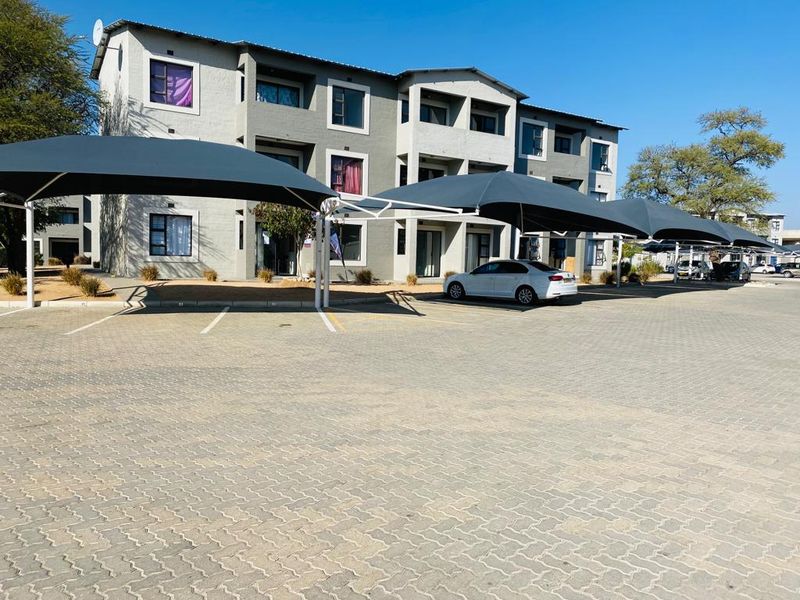 Exterior view of a multi-story apartment complex featuring a paved parking area with installed shade cloth carports.