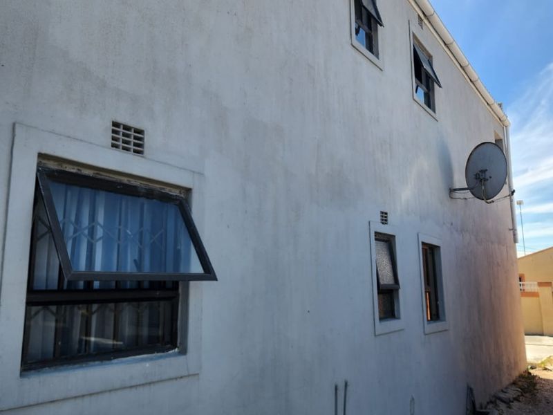 Side elevation of the property featuring plastered walls, top-hung windows with security bars, and external plumbing fixtures.