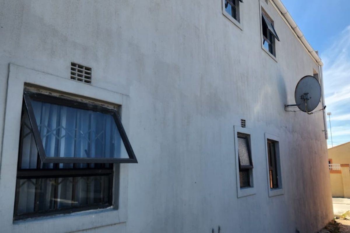 Side elevation of the property featuring plastered walls, top-hung windows with security bars, and external plumbing fixtures.