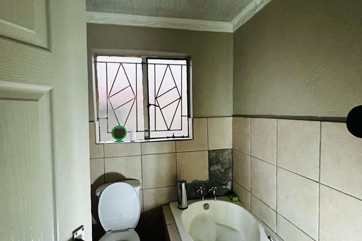 A compact bathroom featuring a bathtub, toilet, and tiled wall finishes, requiring some maintenance and cosmetic updates.