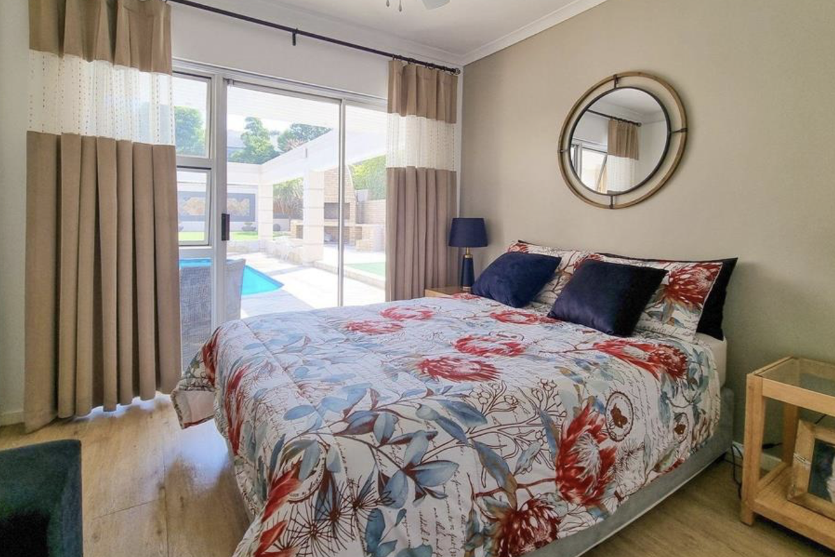 A well-maintained bedroom featuring laminate flooring, built-in cupboards, and a sliding glass door providing direct access to the outdoor pool area.