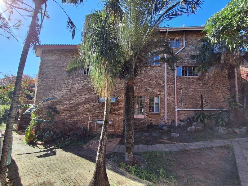 Rear view of a multi-story face brick house featuring steel-framed windows, paved pathways, and established garden landscaping.