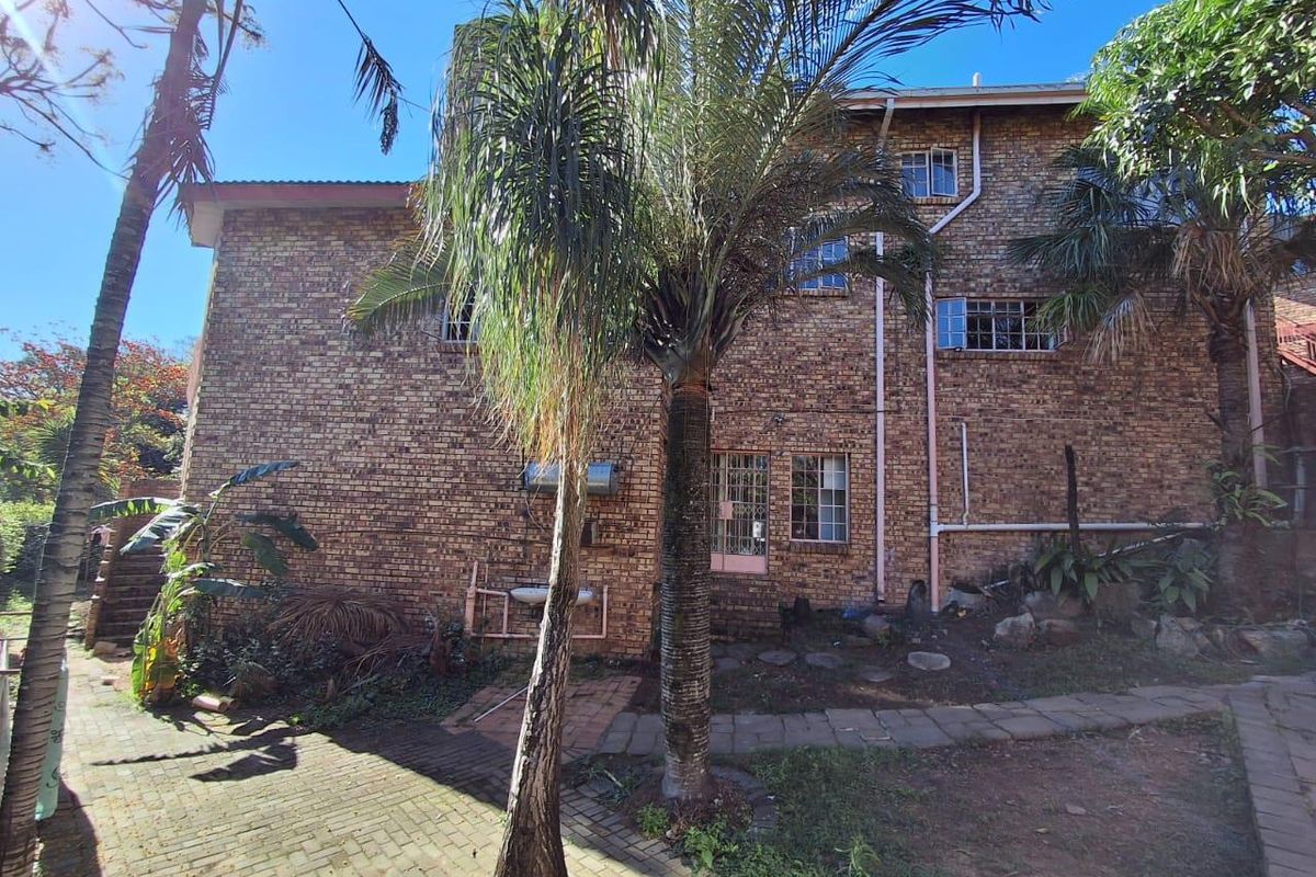 Rear view of a multi-story face brick house featuring steel-framed windows, paved pathways, and established garden landscaping.