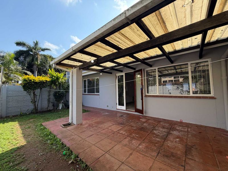 A covered outdoor patio area featuring tiled flooring, a timber-framed translucent roof, and direct access to the garden through glass doors.