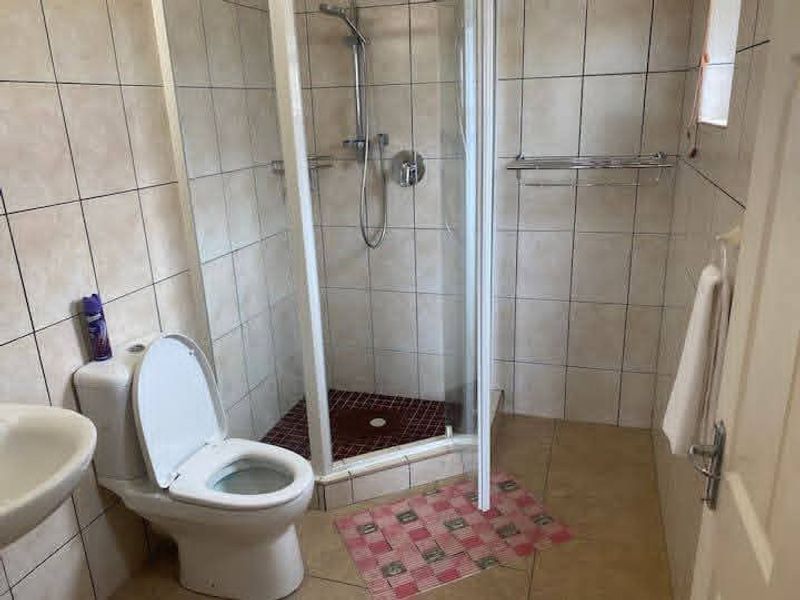 A functional bathroom featuring a corner shower enclosure, tiled walls and flooring, and standard sanitary fixtures.