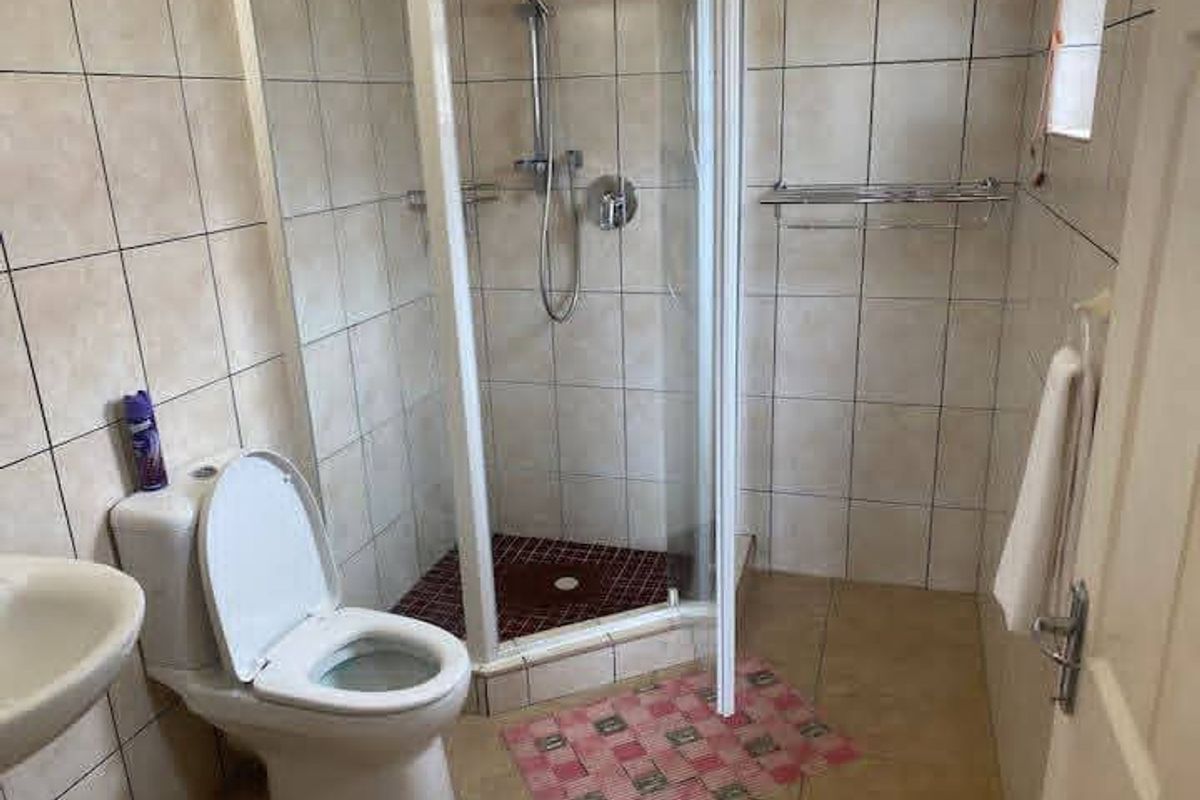 A functional bathroom featuring a corner shower enclosure, tiled walls and flooring, and standard sanitary fixtures.